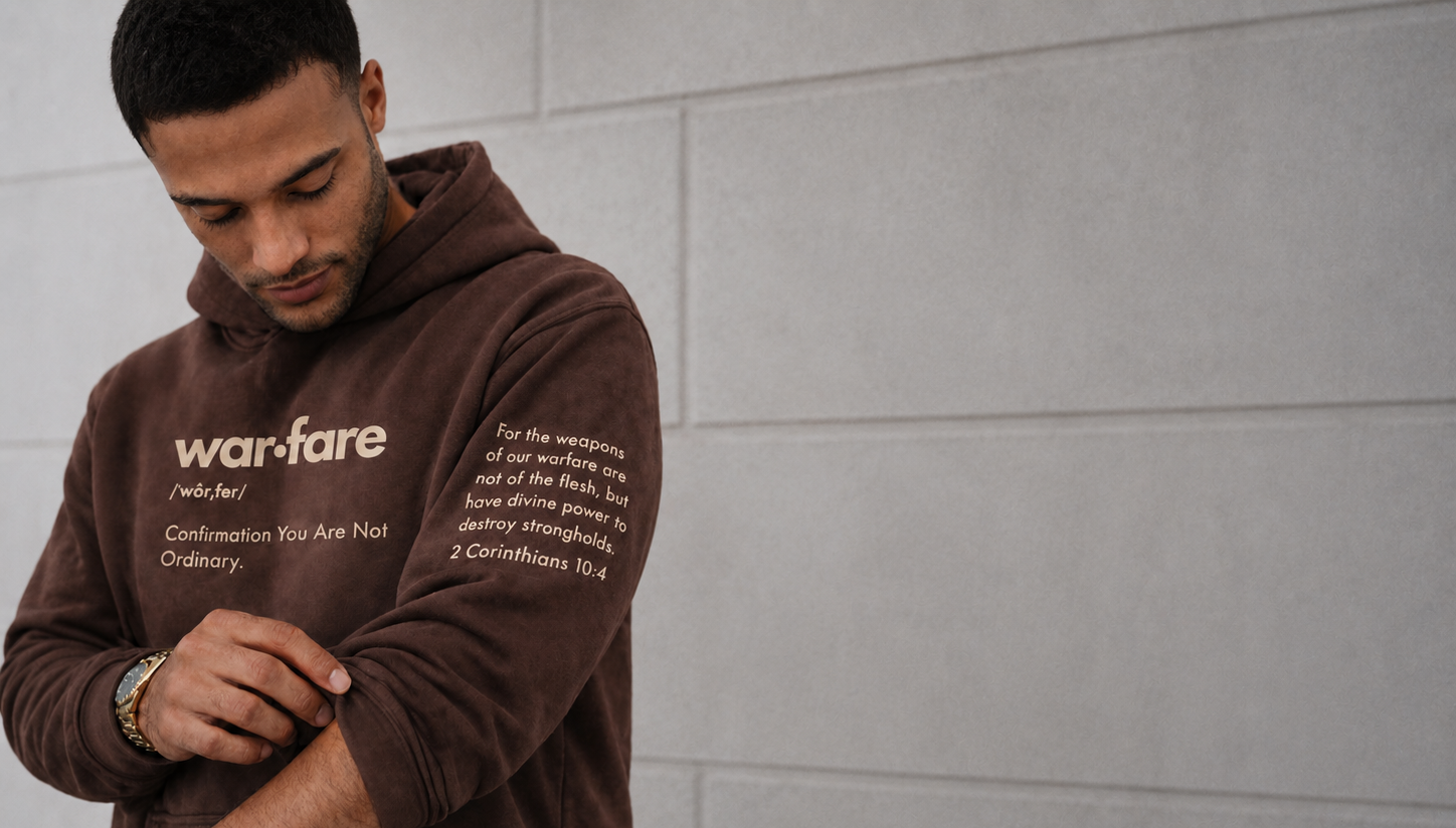 Man wearing a brown hoodie with text, standing against a gray tiled wall.