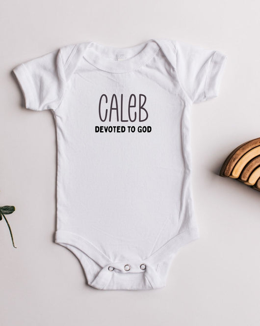 White baby onesie with 'CALEB DEVOTED TO GOD' text on a light background
