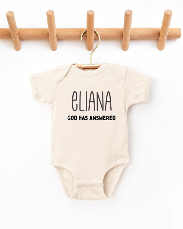 Beige baby onesie with 'ELIANA GOD HAS ANSWERED' text on a white background