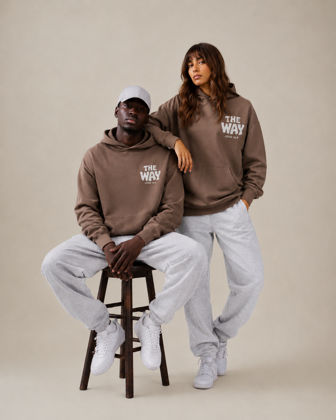 Two people wearing matching brown hoodies with 'THE WAY' text on a beige background