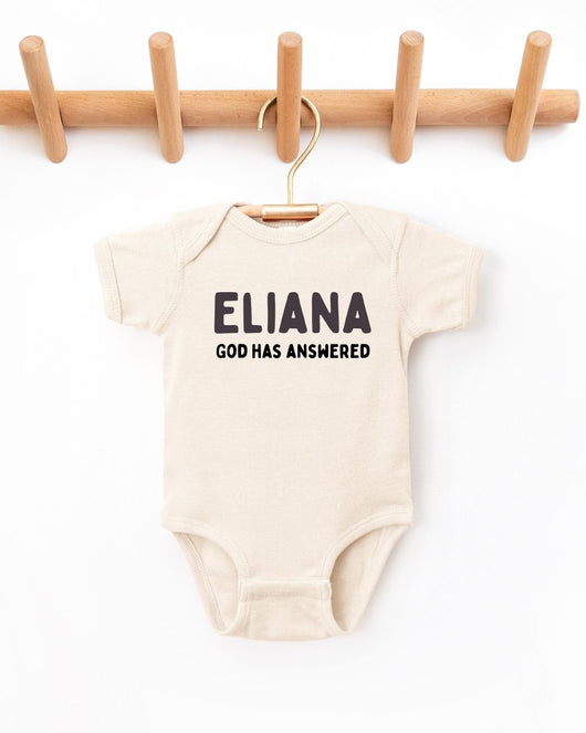 Beige baby onesie with 'ELIANA GOD HAS ANSWERED' text on a white background