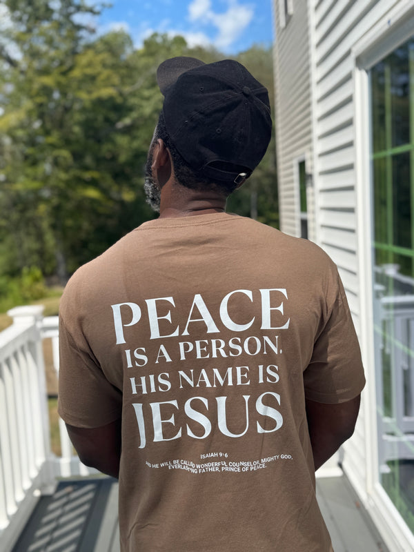 Person wearing a brown t-shirt with a religious message on a porch.